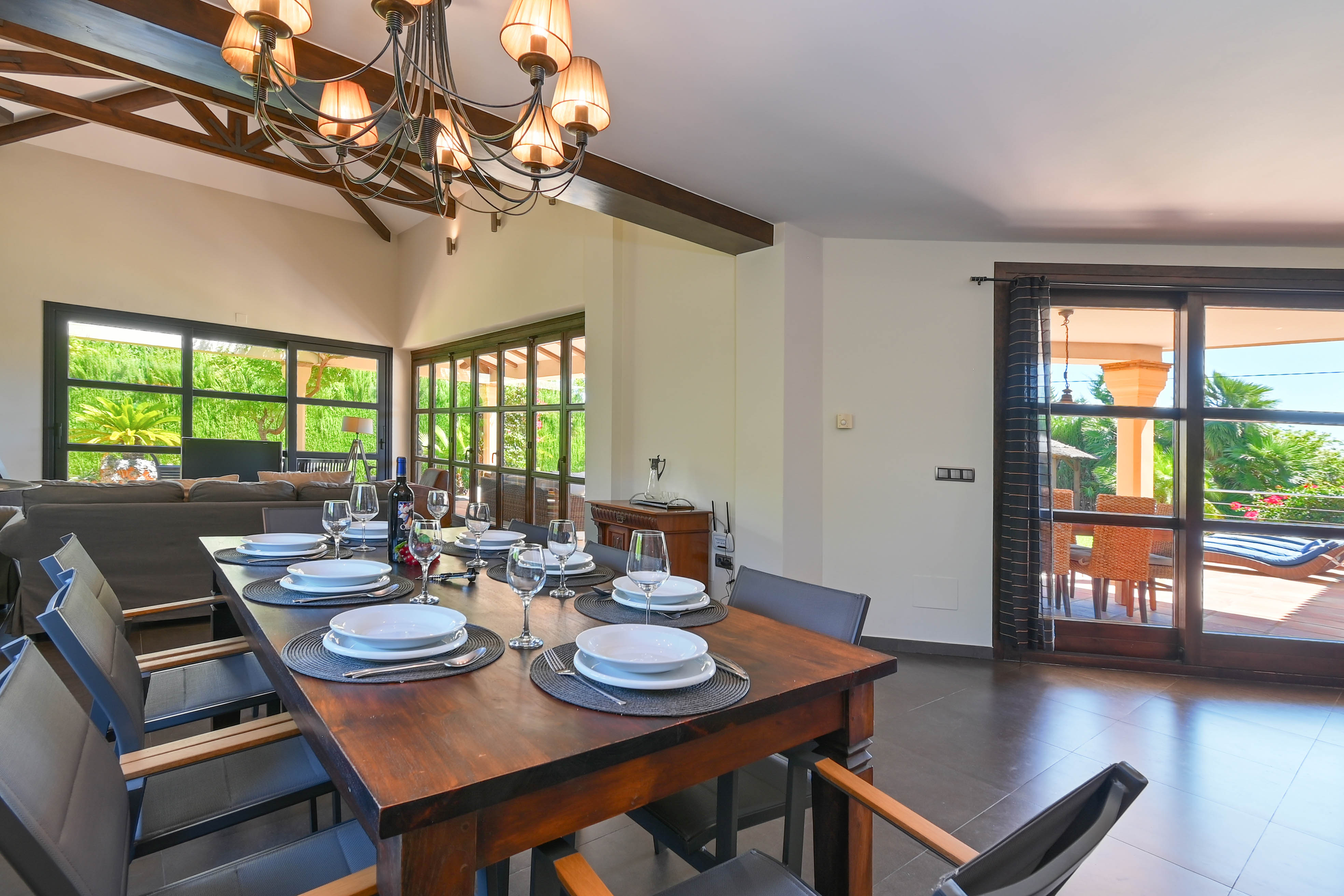 Salle à manger lumineuse avec table en bois foncé et vue sur la terrasse avec piscine.