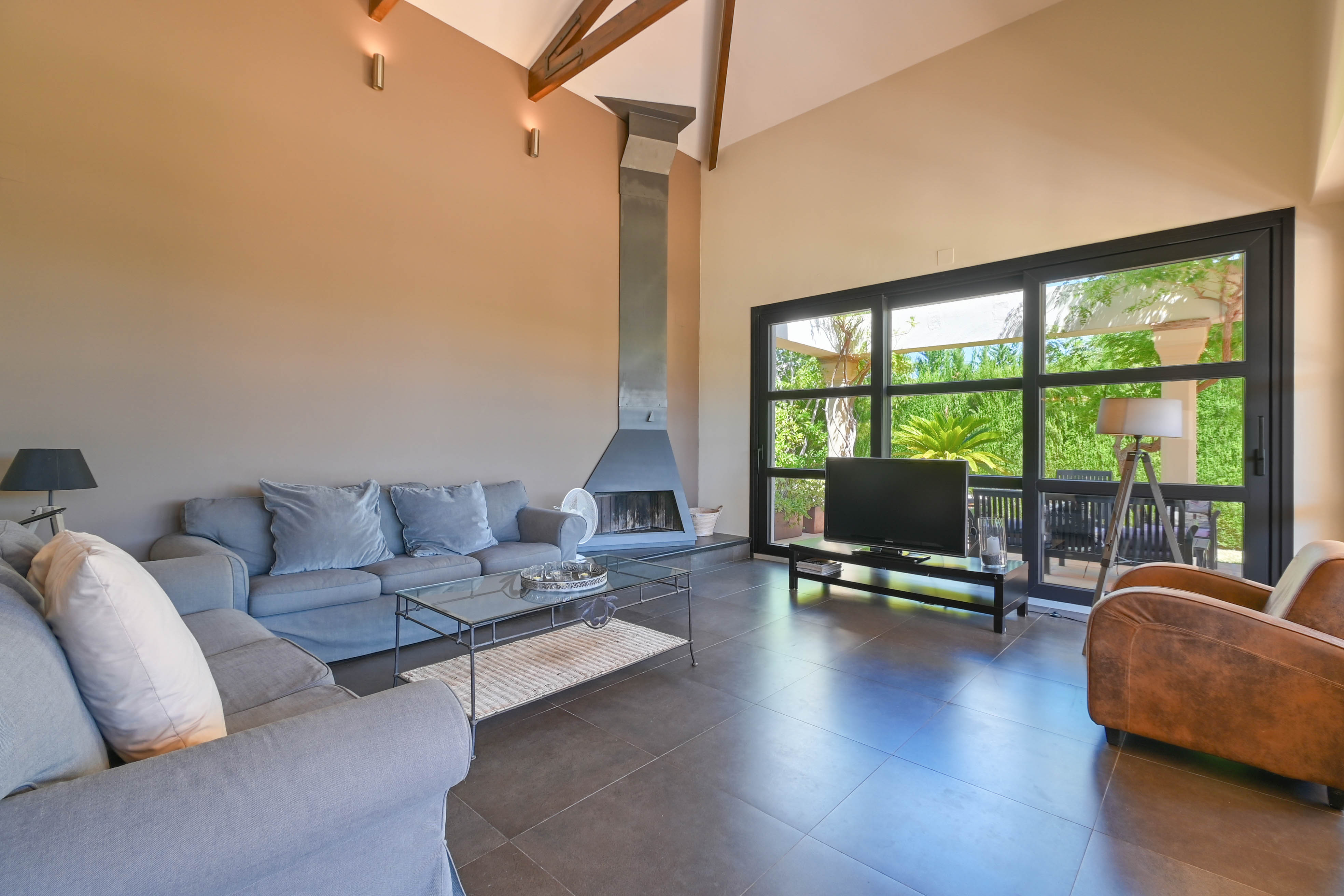 Salon spacieux avec cheminée en métal, canapé gris et grandes fenêtres donnant sur le jardin à Denia, Costa Blanca.