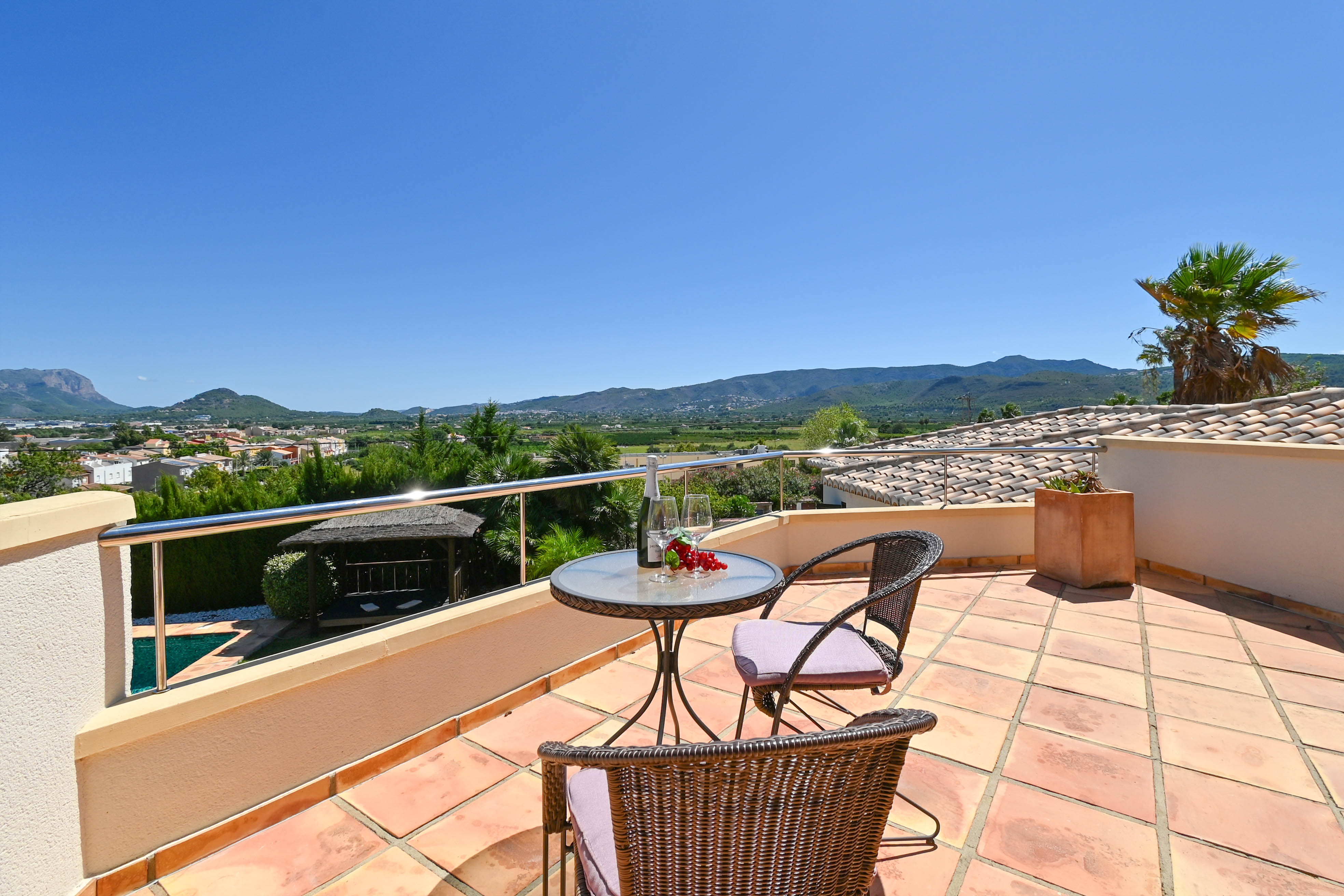 Terrasse avec table en verre, chaises en osier et vue sur la vallée et les montagnes.