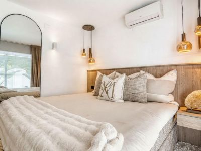 Chambre avec tête de lit en bois, luminaires suspendus dorés et miroir en pied.