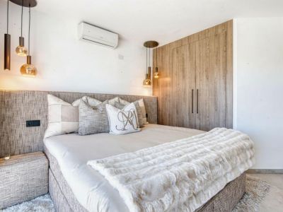 Chambre avec tête de lit texturée, suspensions design et armoire encastrée en bois clair.