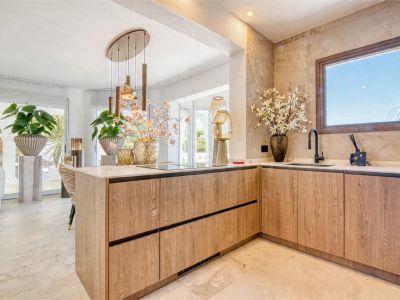Détail de la cuisine avec îlot central en bois clair et plan de travail en marbre. Éclairage suspendu et plantes ornementales.