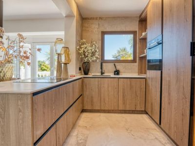 Détail de la cuisine avec meubles en bois clair et plan de travail en marbre, éclairée par la lumière naturelle.