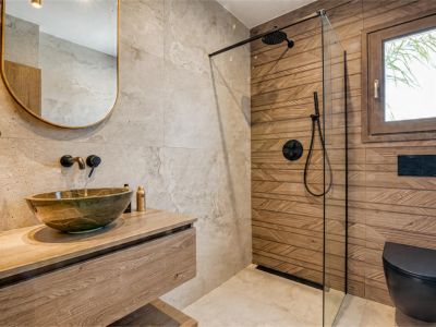 Détail de la salle de bain avec vasque en pierre sur comptoir en bois et douche avec paroi en verre.