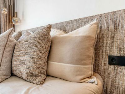 Détail du lit avec tête de lit en texture tissée et coussins décoratifs dans des tons neutres. Prise électrique intégrée à la tête de lit.
