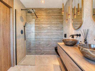 Salle de bain élégante avec vasques en pierre et douche vitrée, soulignant le revêtement mural à motifs géométriques.
