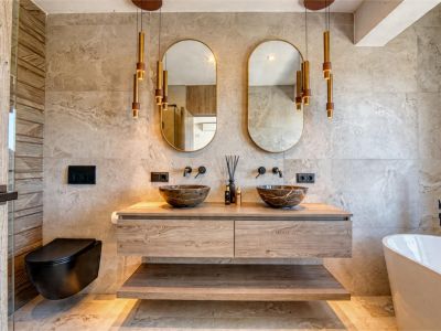 Salle de bain élégante avec vasques en pierre, meuble-lavabo suspendu en bois et suspensions dorées. Design moderne avec carrelage neutre.