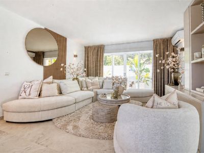 Salon lumineux avec canapé modulable beige, tapis moelleux et miroir rond décoratif.