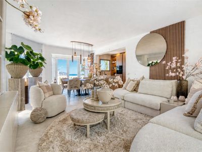 Salon lumineux avec décor neutre, tapis moelleux et accès à la salle à manger avec vue sur la mer.