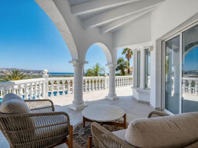 Terrasse couverte avec arcades en pierre, mobilier en rotin et vue panoramique sur la mer Méditerranée.