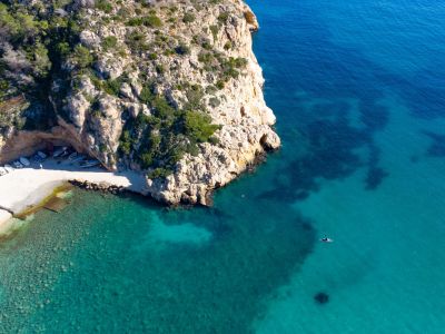 Vue aérienne d'une crique rocheuse avec des bateaux sur la plage et des eaux turquoises.
