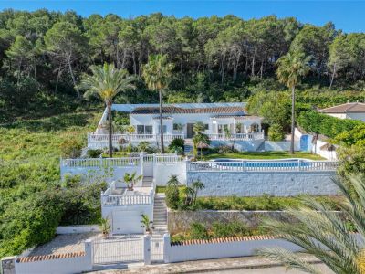 Vue extérieure de la villa à Piver, Jávea, mettant en valeur sa façade blanche, sa piscine et ses jardins en terrasses avec végétation méditerranéenne.