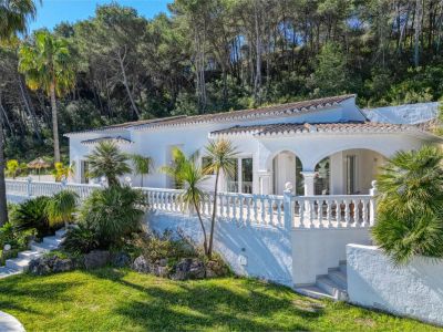 Vue extérieure de la villa avec terrasse couverte, balustrade et jardin paysager avec végétation méditerranéenne.
