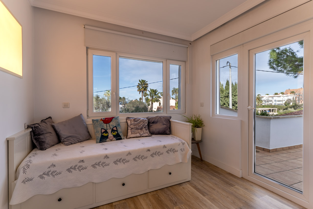 Chambre lumineuse avec lit de repos, vue sur l'extérieur et accès à la terrasse.