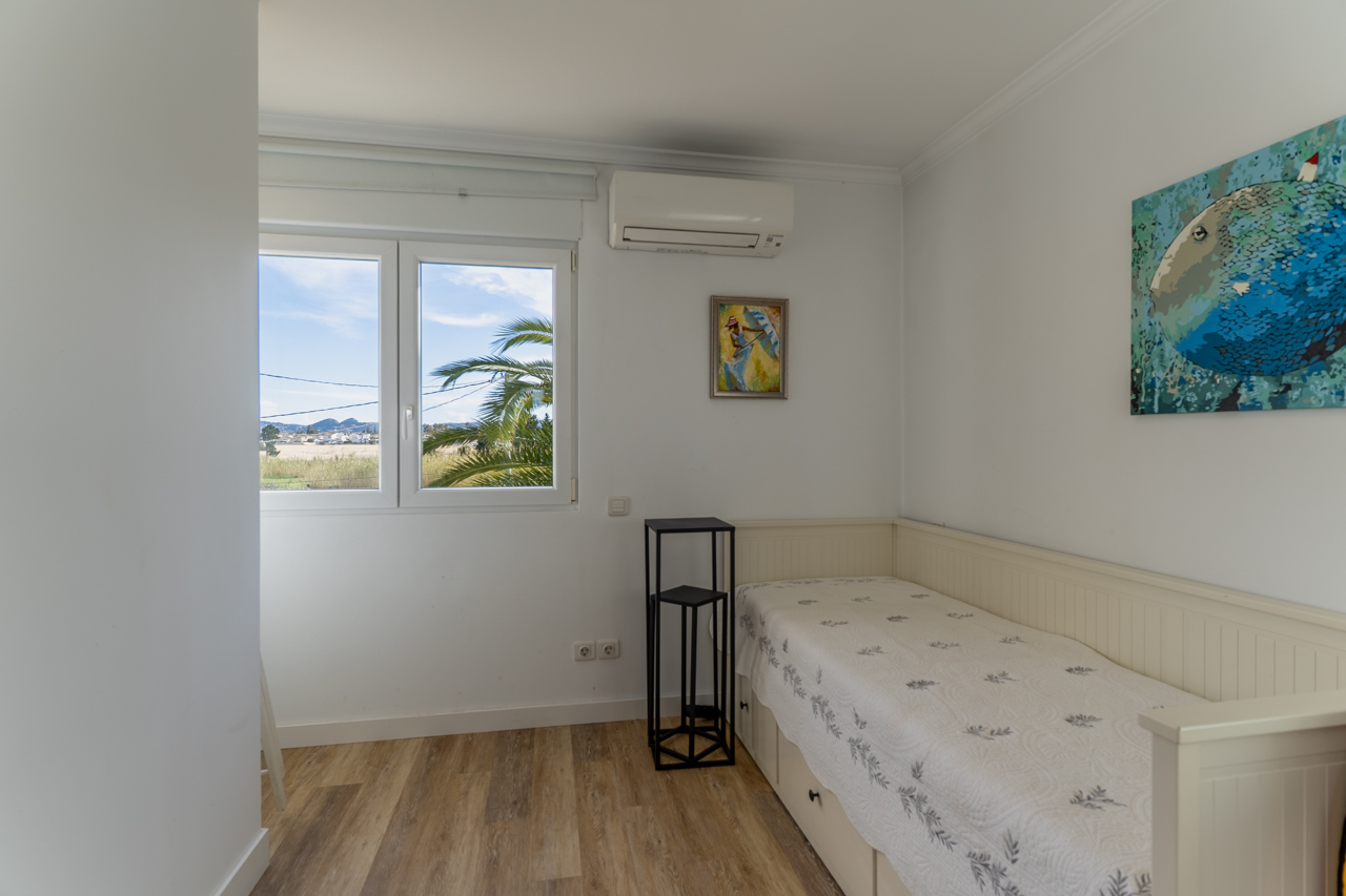 Chambre lumineuse avec lit simple, décor moderne et vue extérieure avec des palmiers.
