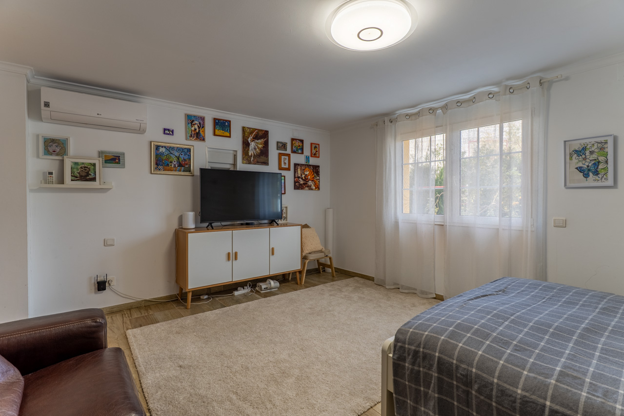 Chambre lumineuse avec tapis moelleux, meuble TV blanc et décoration artistique éclectique au mur.