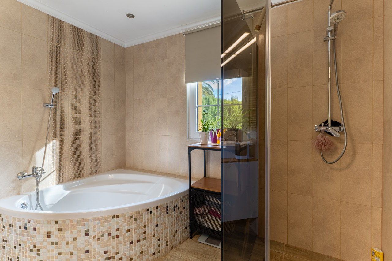 Détail de la salle de bain avec baignoire d'angle en mosaïque et douche vitrée.