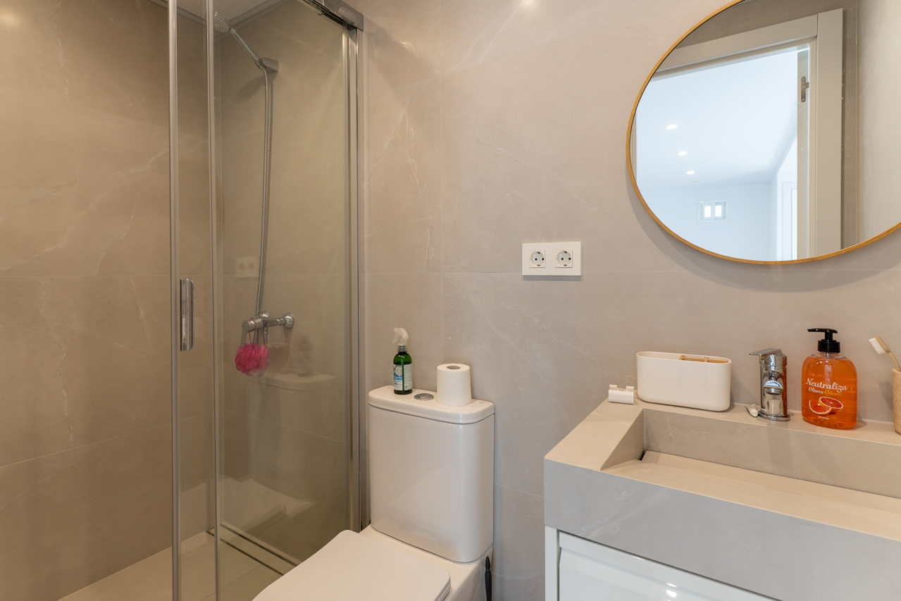 Détail de la salle de bain avec douche en verre, lavabo moderne et miroir circulaire à cadre doré.