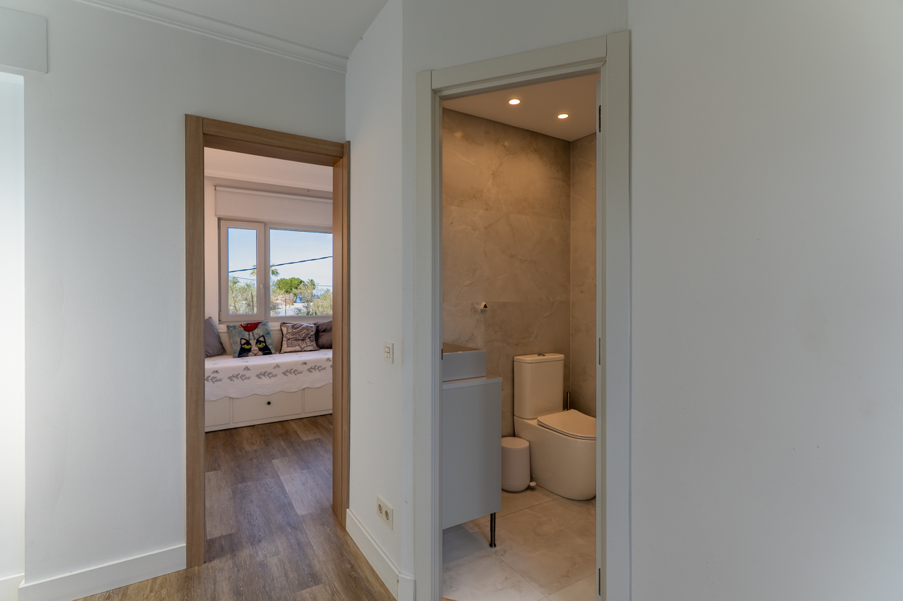 Détail du couloir avec accès à une salle de bain en marbre et une chambre lumineuse.