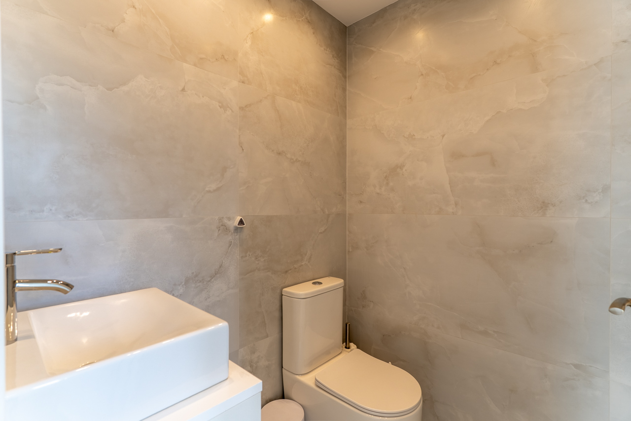 Détail d'une salle de bain moderne avec murs en carrelage veiné, vasque carrée sur comptoir blanc et toilettes contemporaines.