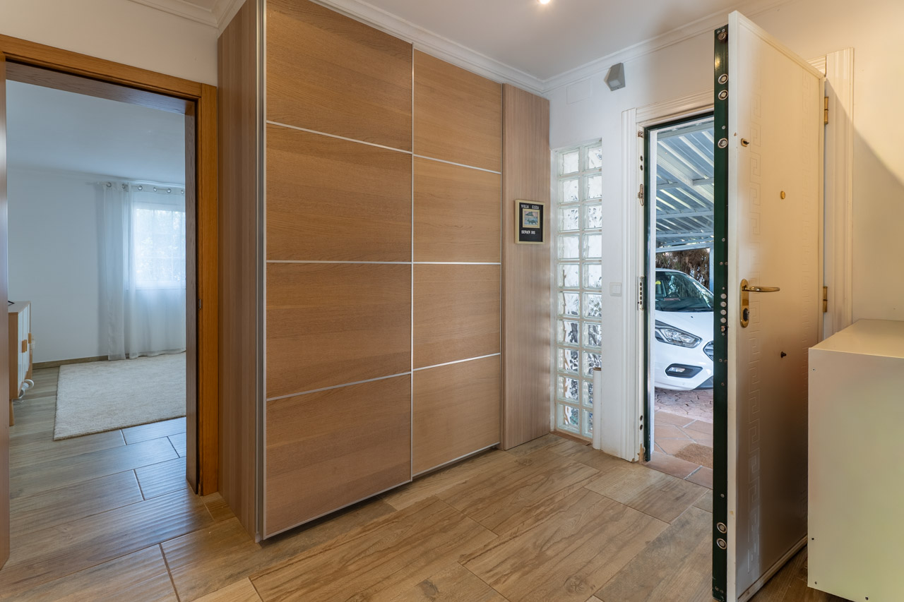 Entrée avec placard intégré en bois clair et porte blindée ouverte sur le garage.