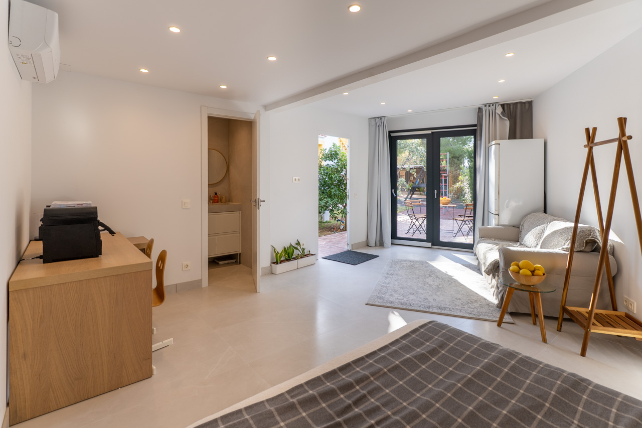 Espace multifonctionnel lumineux avec accès au jardin, salle de bain attenante et mobilier fonctionnel aux tons neutres.