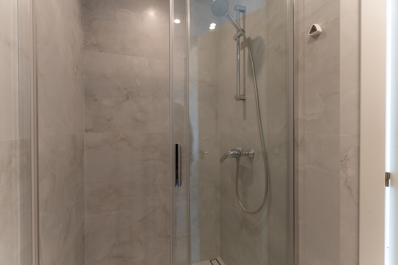 Gros plan sur la douche avec paroi en verre et carrelage en céramique imitation marbre.