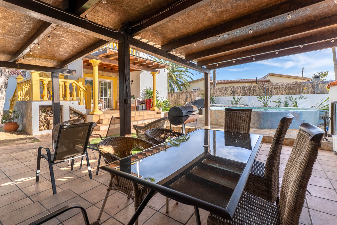 Salle à manger extérieure couverte avec barbecue et piscine dans le jardin de la villa.