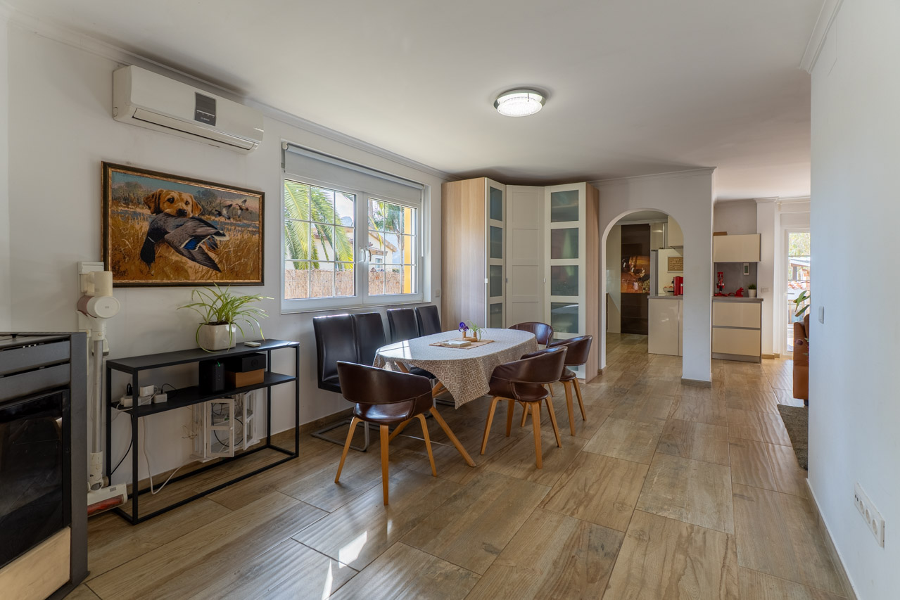 Salle à manger lumineuse avec plancher imitation bois, table ovale et six chaises en cuir marron.