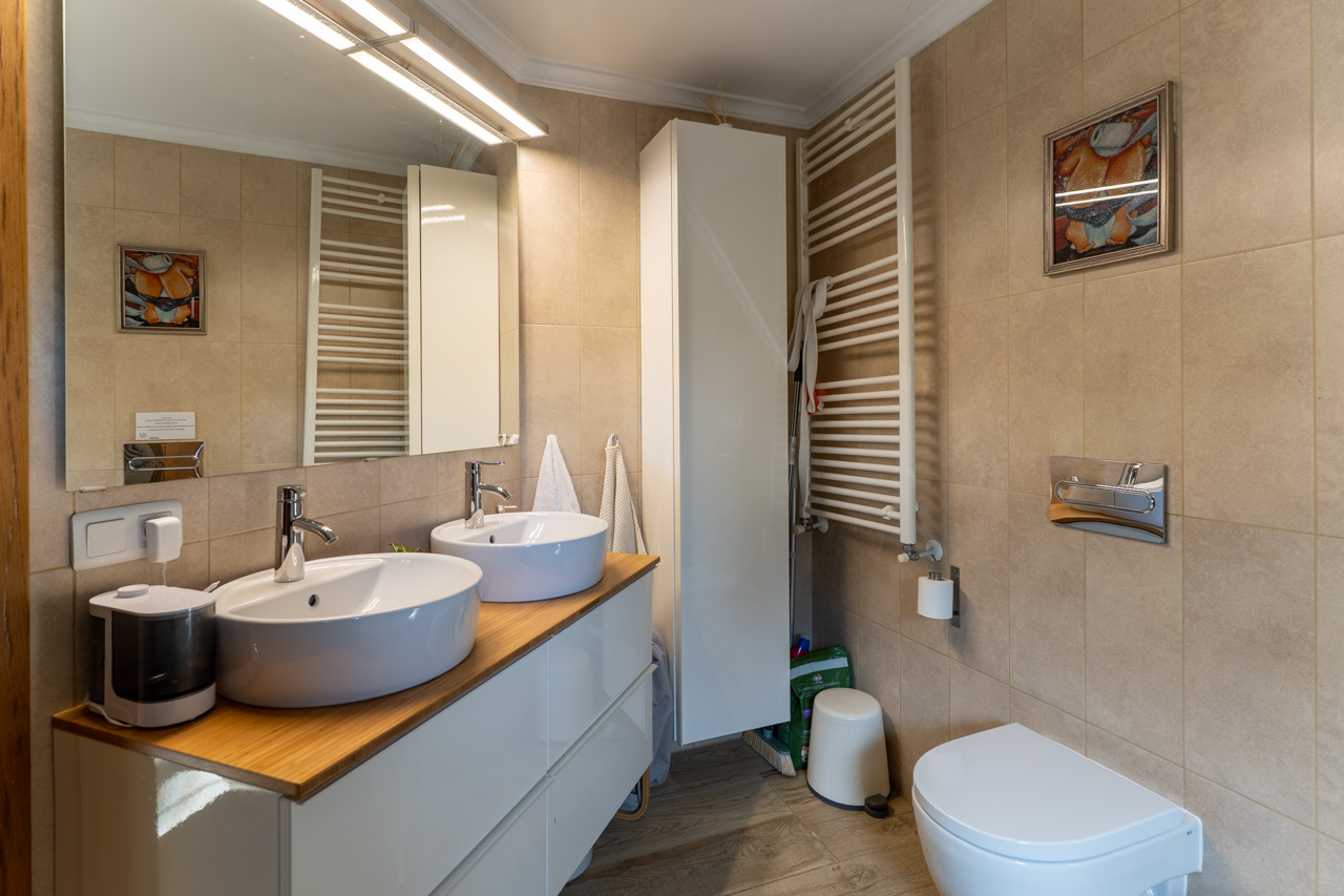 Salle de bain avec double vasque sur comptoir en bois, sèche-serviettes chauffant et carrelage céramique sable.