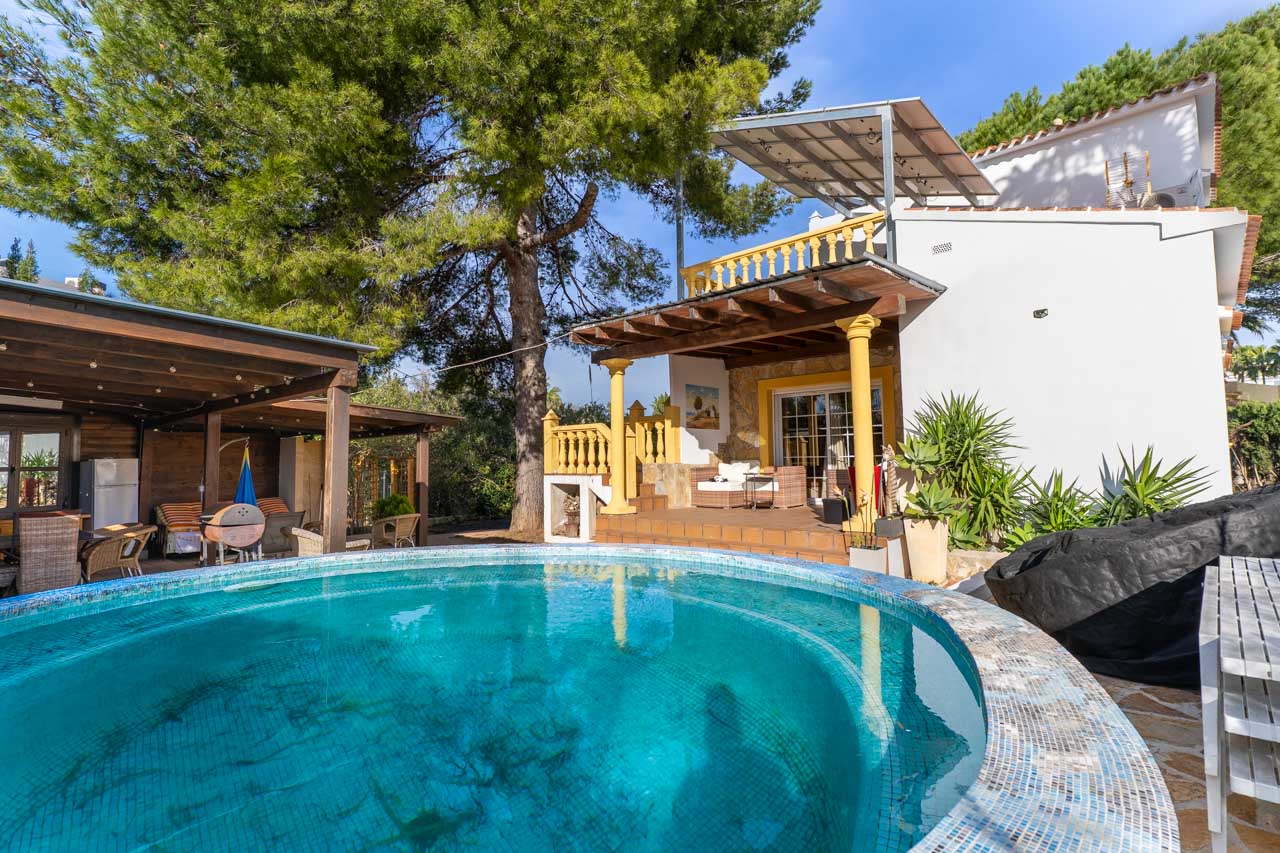 Vue de la piscine en mosaïque bleue et de la terrasse couverte avec des piliers jaunes.