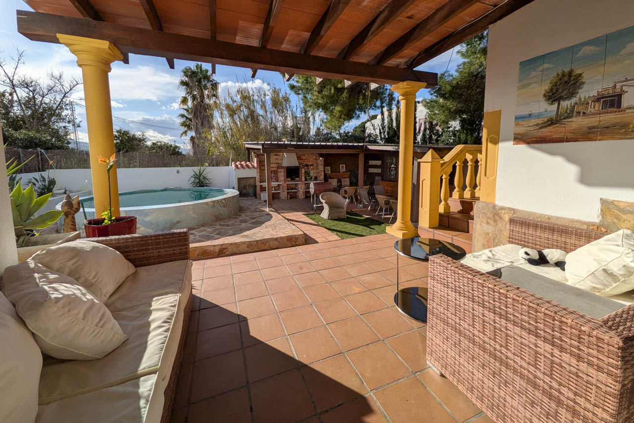 Vue du patio avec piscine, espace barbecue et coin salon couvert avec meubles en rotin.