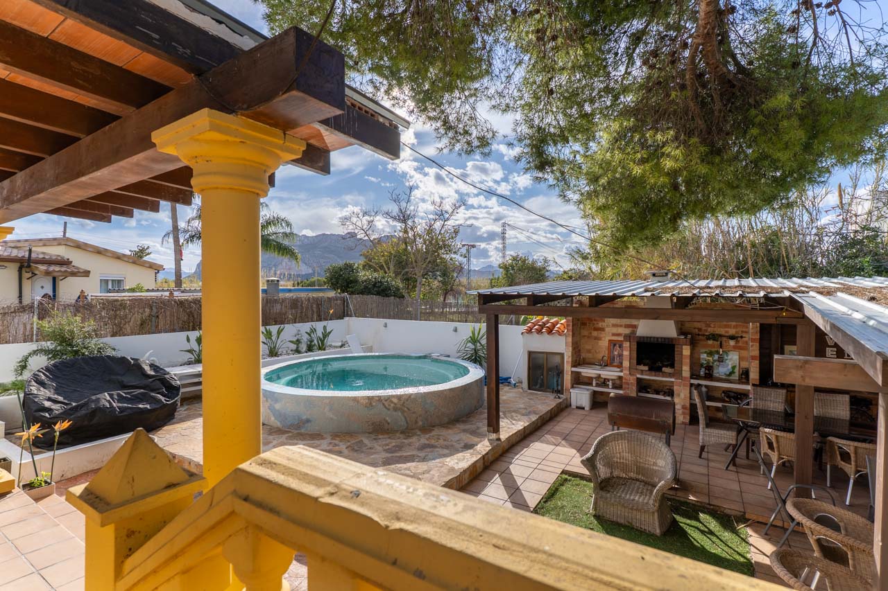 Vue sur la piscine avec barbecue couvert, depuis la terrasse avec rambarde jaune.
