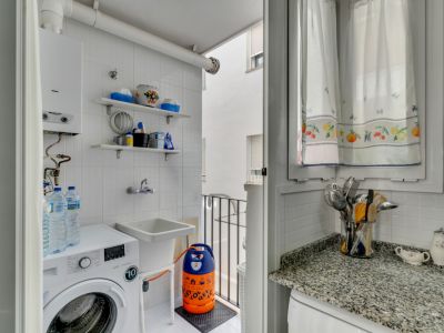 Buanderie avec machine à laver, évier et étagères carrelées en blanc. Fenêtre avec rideaux à motifs.