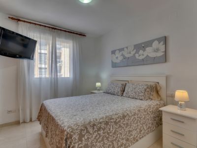 Chambre lumineuse avec lit double, tables de chevet blanches et TV murale.