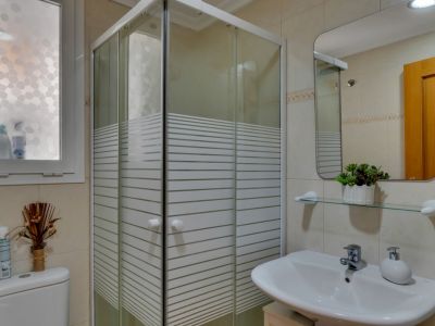 Détail de la salle de bain avec cabine de douche d'angle et lavabo blanc avec miroir rectangulaire.