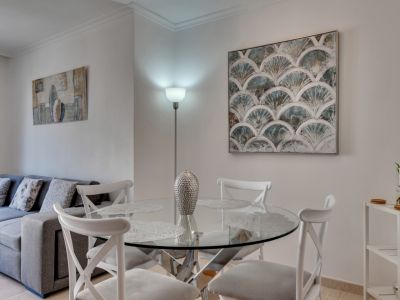 Salle à manger lumineuse avec table ronde en verre et chaises blanches, complétée par de l'art moderne et un lampadaire.