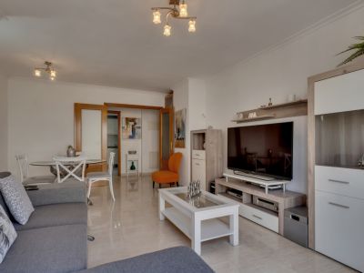 Salon lumineux avec carrelage au sol, canapé gris et mobilier moderne dans des tons neutres et blancs.