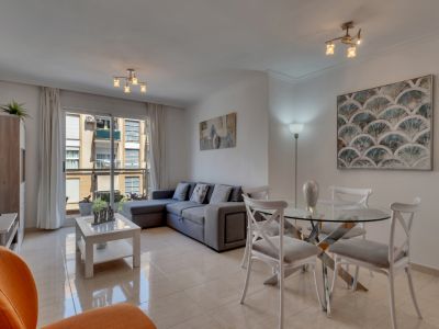 Salon-salle à manger lumineux avec table en verre, canapé d'angle gris et accès au balcon avec vue urbaine.