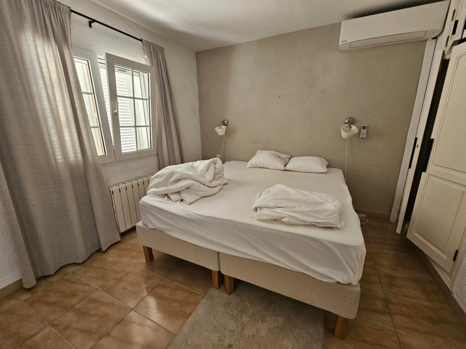 Chambre avec lit double, rideaux en lin et sol en carrelage rustique.