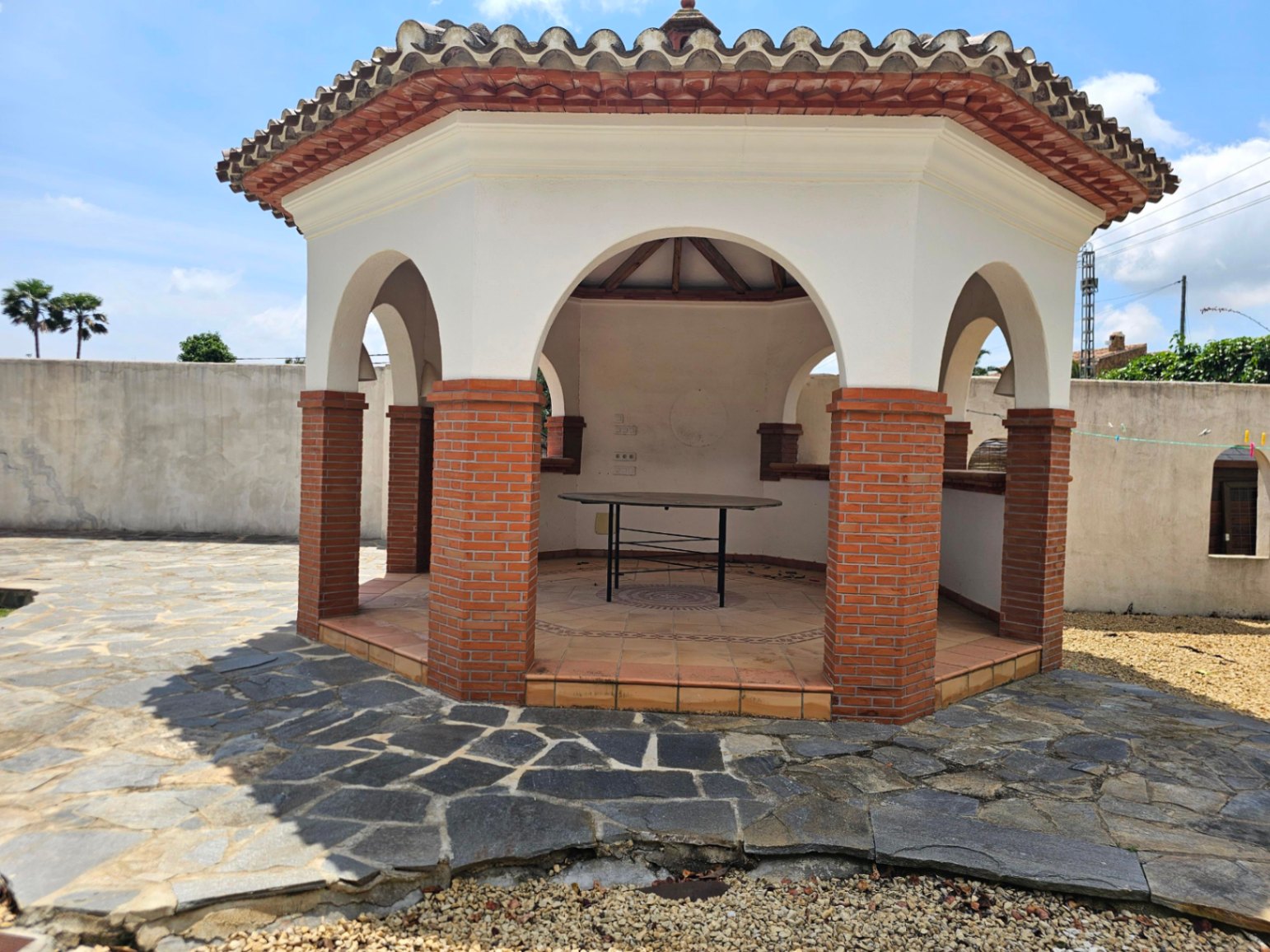 Gazébo extérieur avec colonnes en brique et sol en pierre irrégulière.