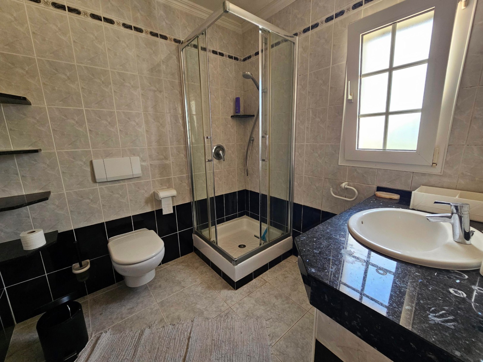 Salle de bain avec douche d'angle et comptoir en granit noir.