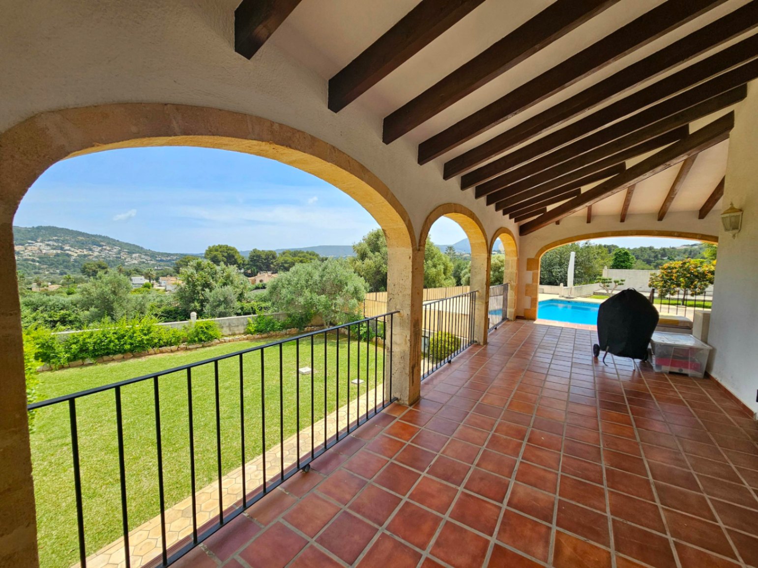 Terrasse couverte avec arches en pierre donnant sur le jardin et la piscine.