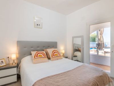 Chambre lumineuse avec tête de lit grise, linge de maison blanc et accès direct à la piscine.