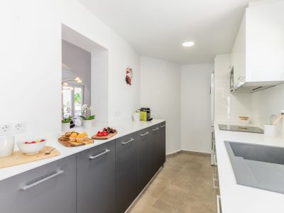 Détail de la cuisine avec comptoir blanc, armoires grises et sol en céramique. Éclairage encastré.