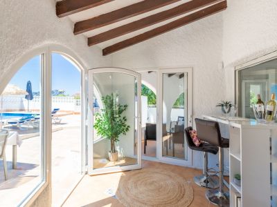 Détail du bar intérieur avec vue sur la piscine et poutres apparentes au plafond.