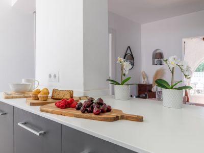 Détail du comptoir de cuisine avec fruits et fleurs, mettant en valeur un design lumineux et moderne.