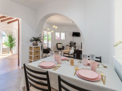 Salle à manger lumineuse avec table dressée dans les tons rose et or, accès à la terrasse et au salon.