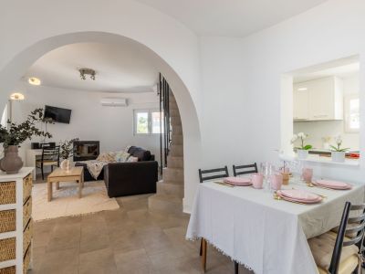 Salle à manger lumineuse avec table dressée dans les tons roses et accès au salon voûté.