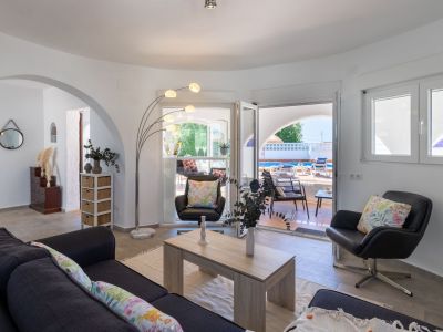 Salon lumineux avec accès terrasse et piscine. Des détails comme la lampe arc et les coussins floraux rehaussent l'espace.